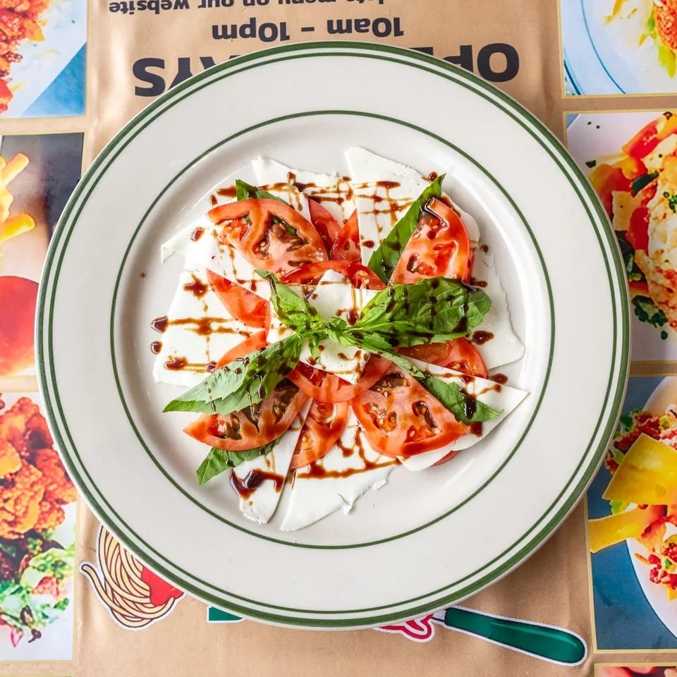 Caprese salad with sliced mozzarella, tomatoes, basil, and balsamic glaze on a white plate.