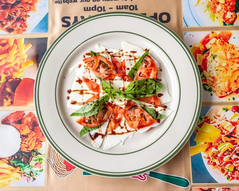 Caprese salad with sliced mozzarella, tomatoes, basil, and balsamic glaze on a white plate.