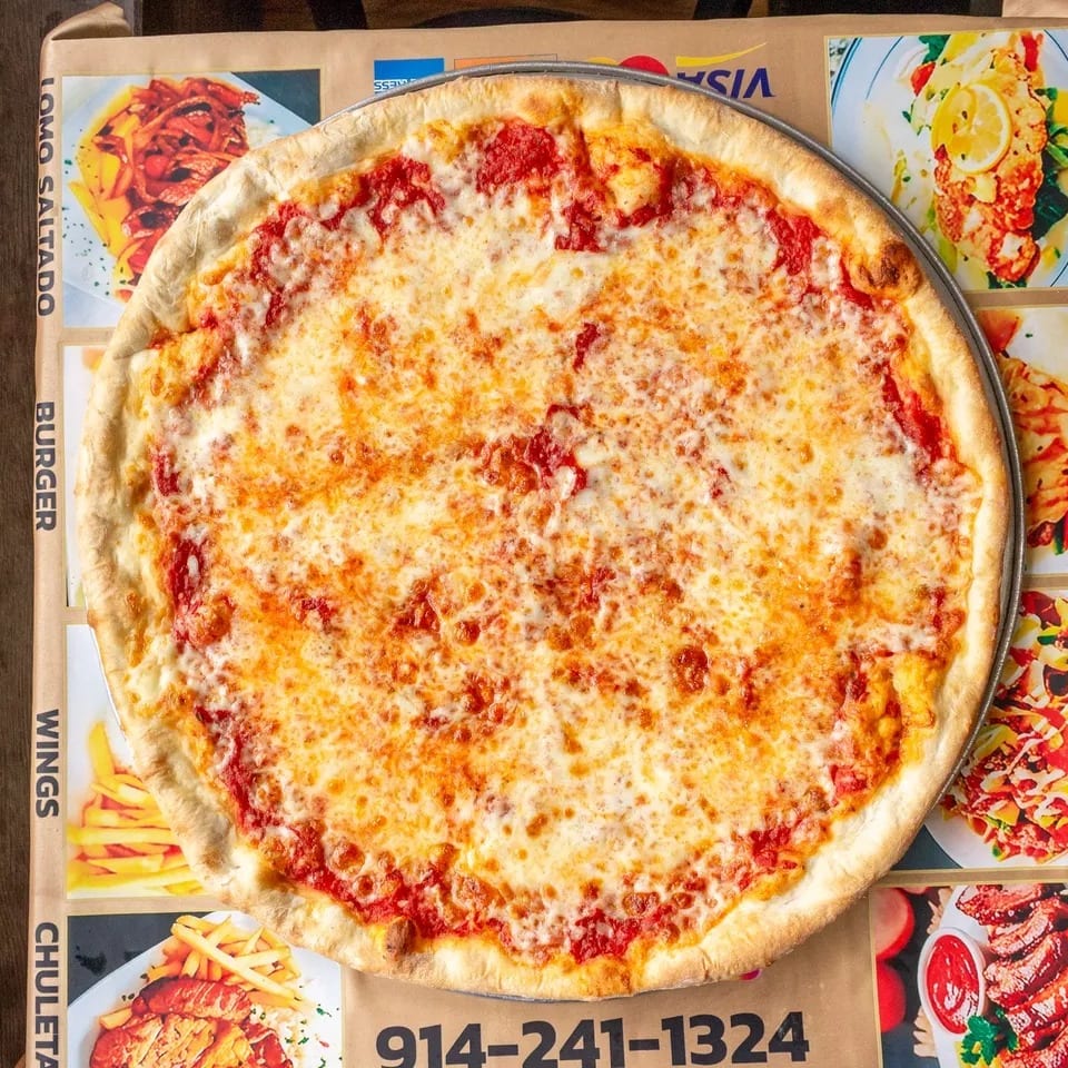 A large, cheesy pizza on a metal pan, sitting on a brown box with a menu and phone number.