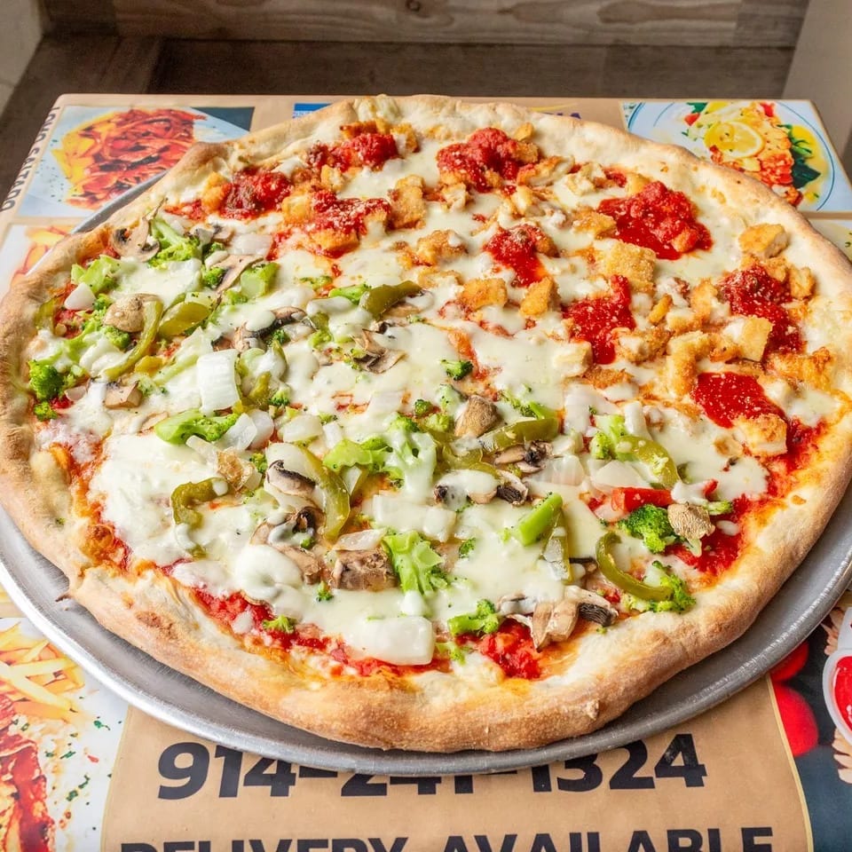 Large pizza with half chicken parmesan and half vegetable toppings on a metal tray.