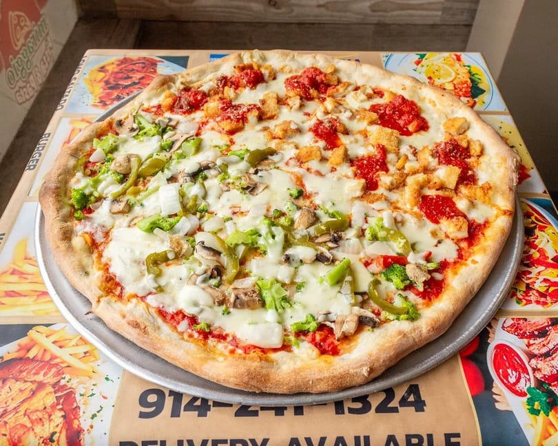 Large pizza with half chicken parmesan and half vegetable toppings on a metal tray.