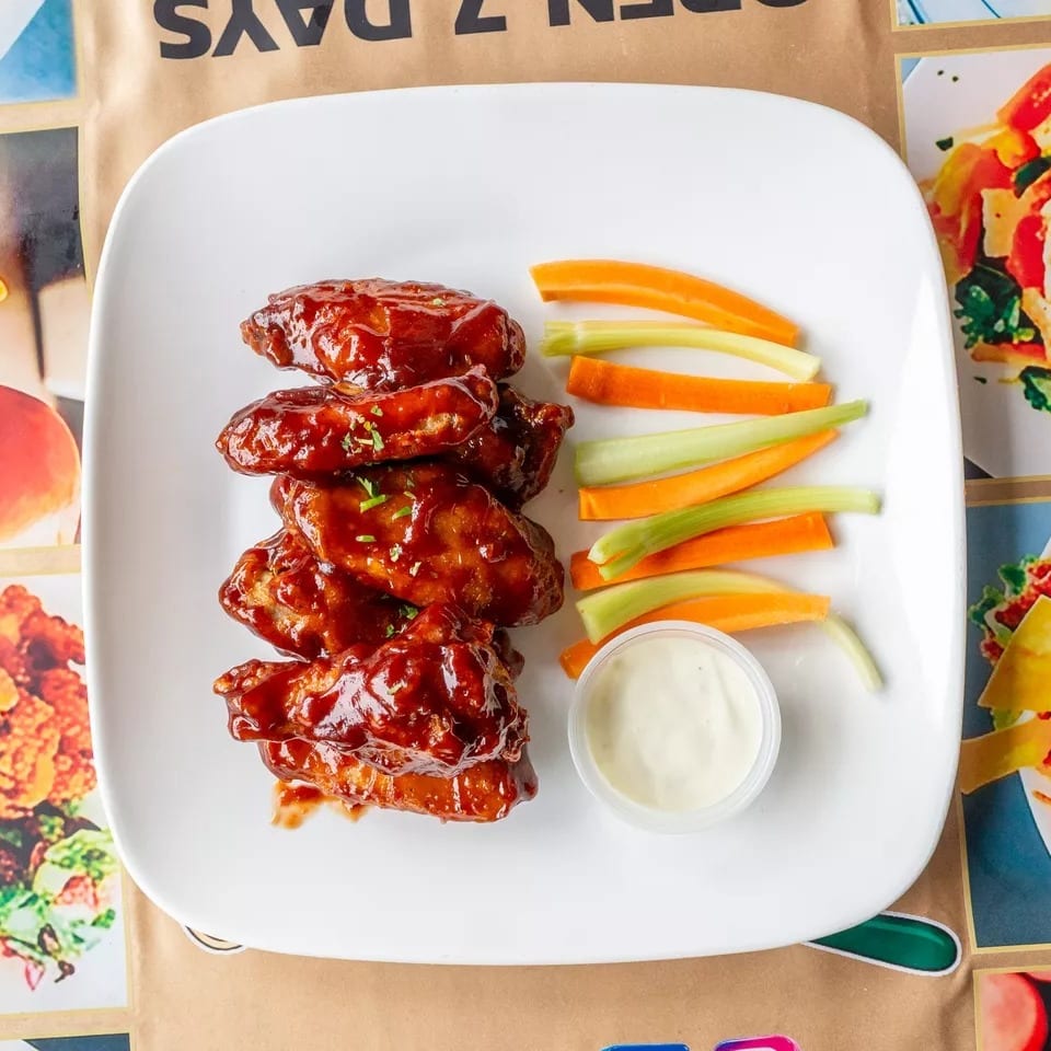 Plate of BBQ chicken wings with celery, carrots, and ranch dip on a restaurant menu.
