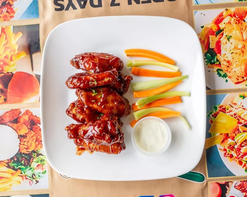 Plate of BBQ chicken wings with celery, carrots, and ranch dip on a restaurant menu.