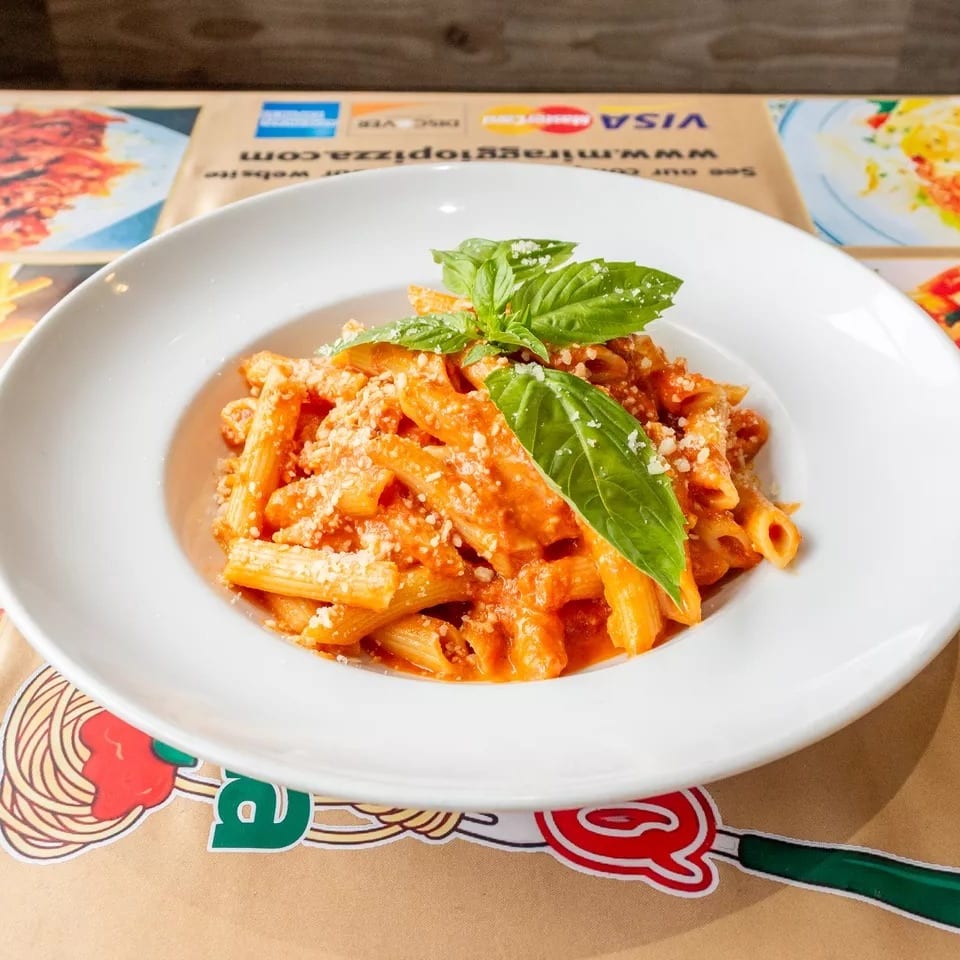 Penne pasta in a creamy red sauce, topped with grated cheese and fresh basil leaves.