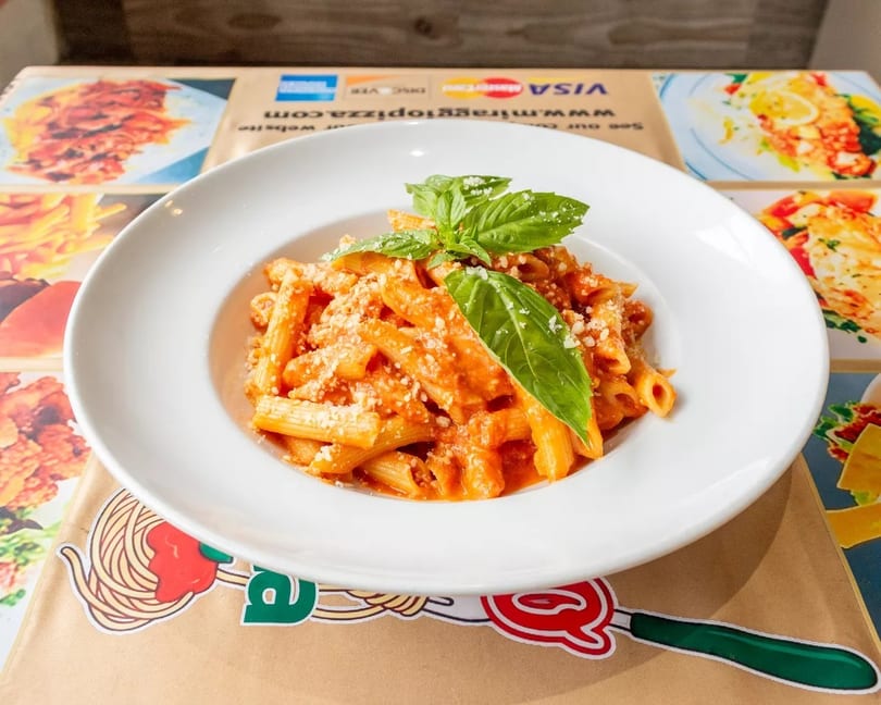 Penne pasta in a creamy red sauce, topped with grated cheese and fresh basil leaves.