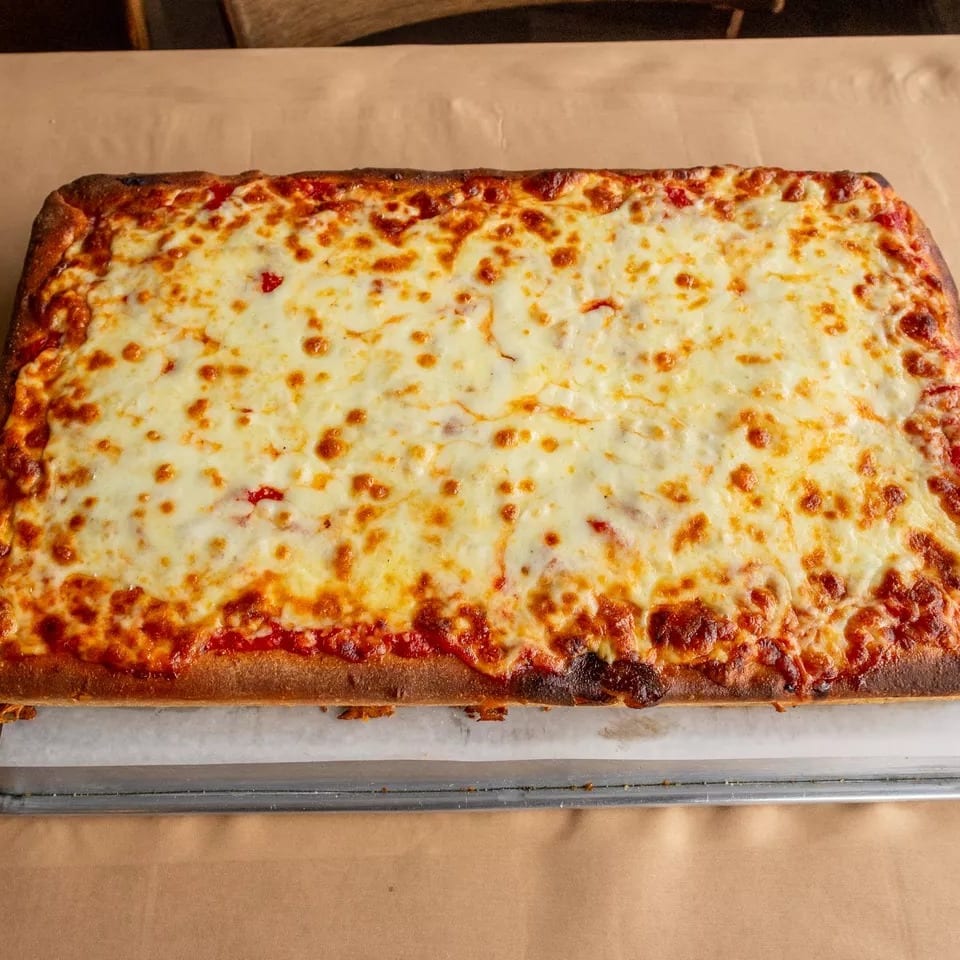 A rectangular cheese pizza with a golden-brown crust on a metal tray with parchment paper.