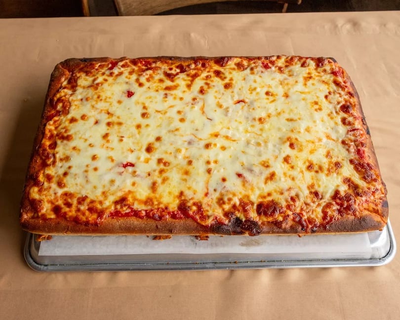 A rectangular cheese pizza with a golden-brown crust on a metal tray with parchment paper.