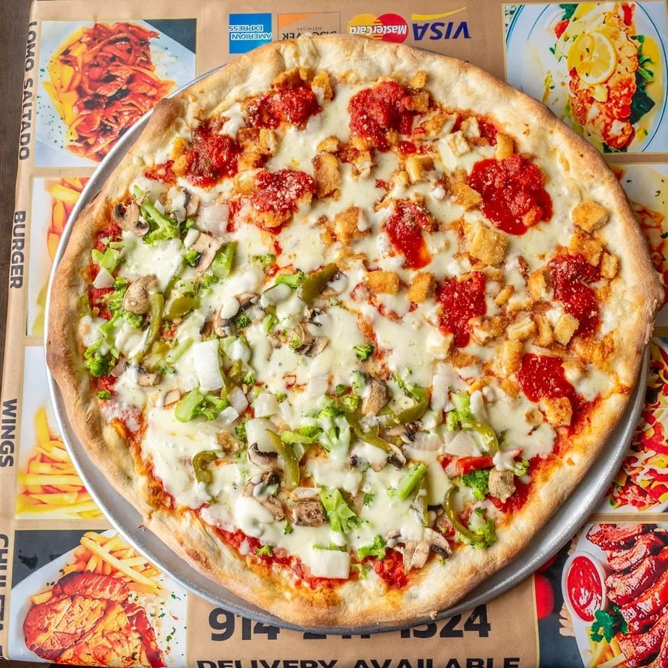 Half vegetable, half chicken and sauce pizza on a metal tray over a restaurant menu.