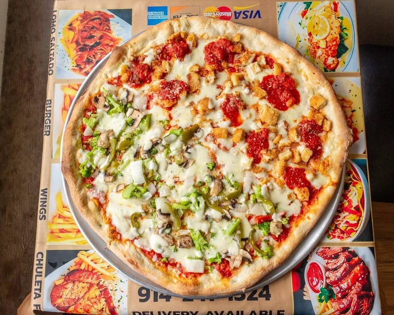 Half vegetable, half chicken and sauce pizza on a metal tray over a restaurant menu.