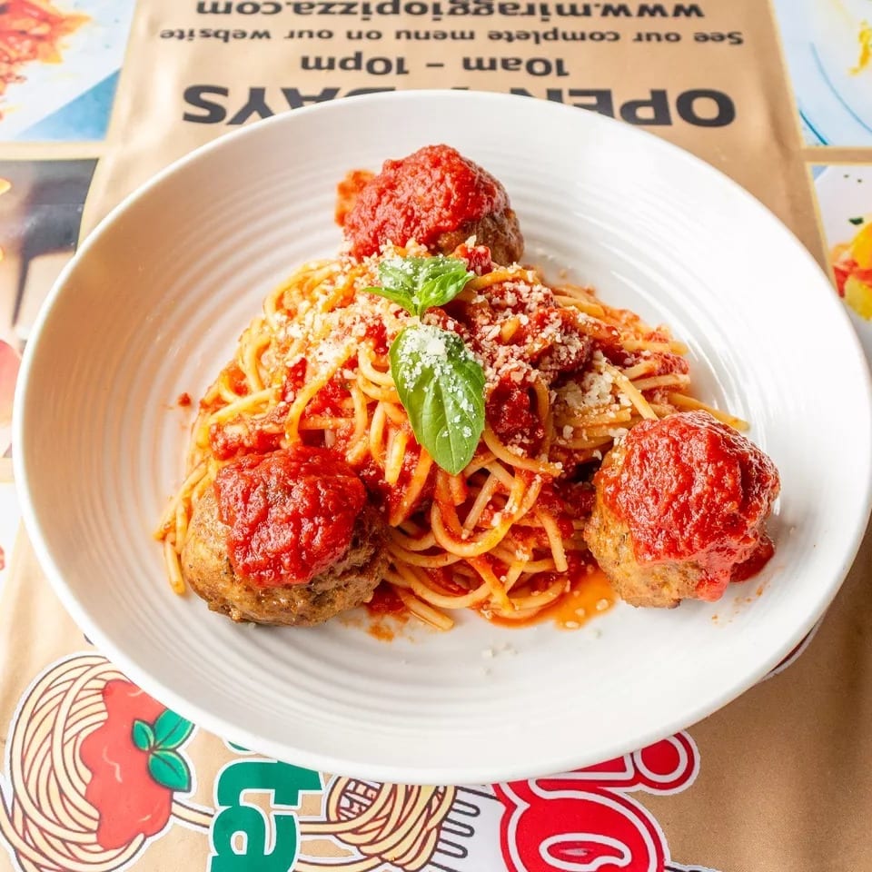 Spaghetti with meatballs, marinara sauce, grated cheese, and fresh basil in a white bowl.