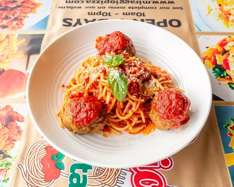 Spaghetti with meatballs, marinara sauce, grated cheese, and fresh basil in a white bowl.